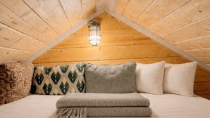 Ein gemütliches Schlafzimmer im Dachgeschoss mit schrägen Holzwänden, einem Bett mit vielen Kissen und einer Hängeleuchte.