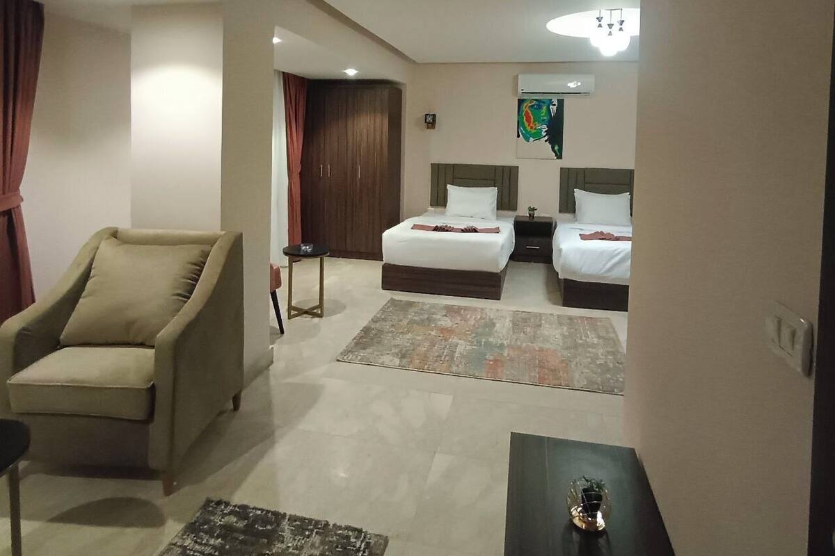 A hotel room with two beds, a sofa, a small table, and a decorative rug.