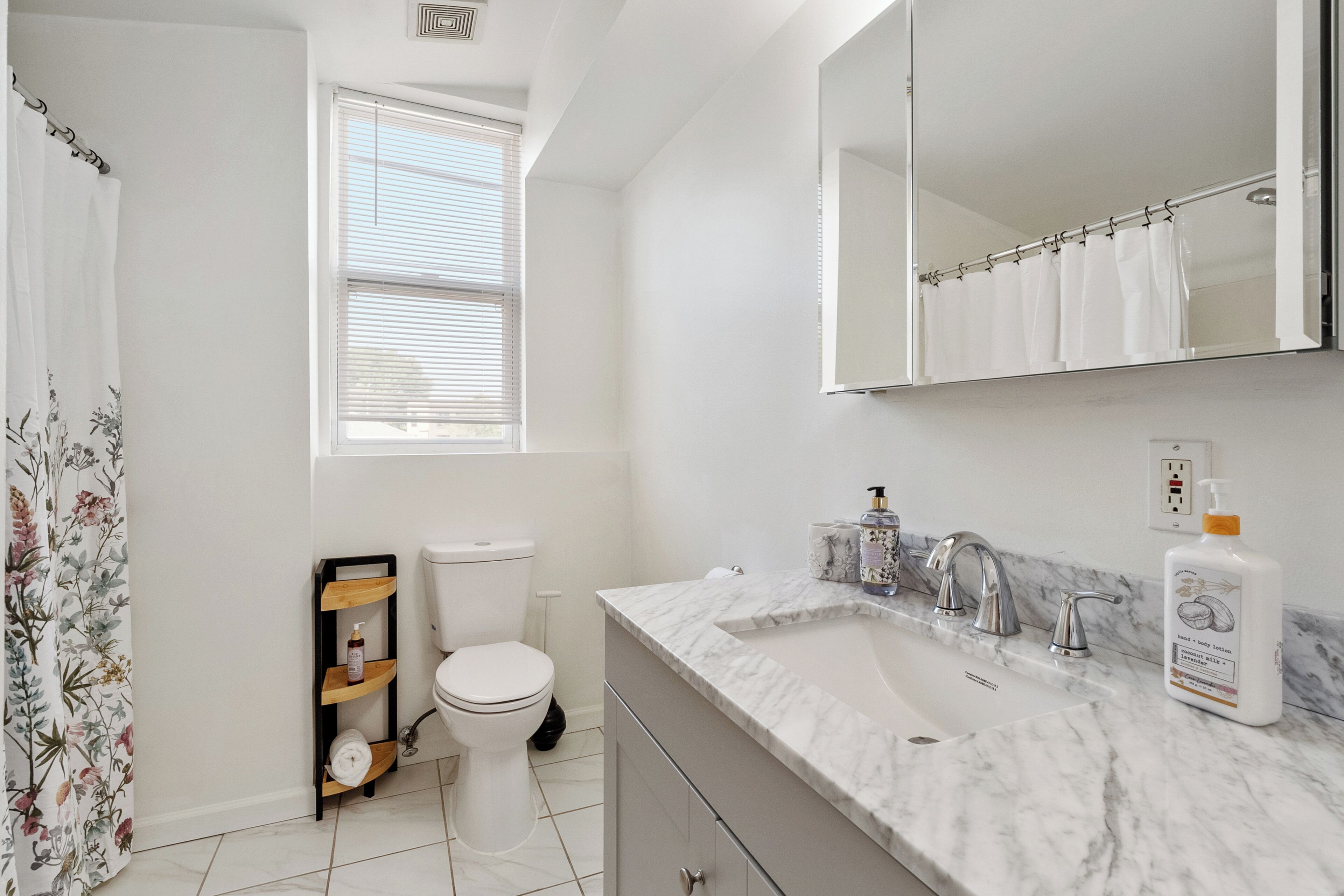 A bathroom with a toilet, a sink with a marble countertop, a mirror, and a shower curtain.