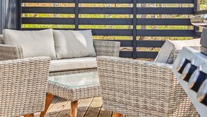 A wicker sofa with cushions, a glass-top table, and a grill on a wooden deck. - Villa sirius 56 by Interhome (Kemiönsaari)