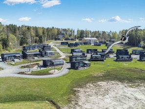 Un barrio residencial moderno con varias casas de dos pisos, una carretera sinuosa y un fondo boscoso.
