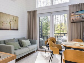 A cozy living room with a grey sofa, a wooden dining table, and a teddy bear on a chair.
