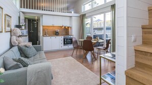 Une cuisine moderne avec des meubles blancs, un coin repas doté d’une table en verre et un espace salon confortable avec un canapé et des coussins.