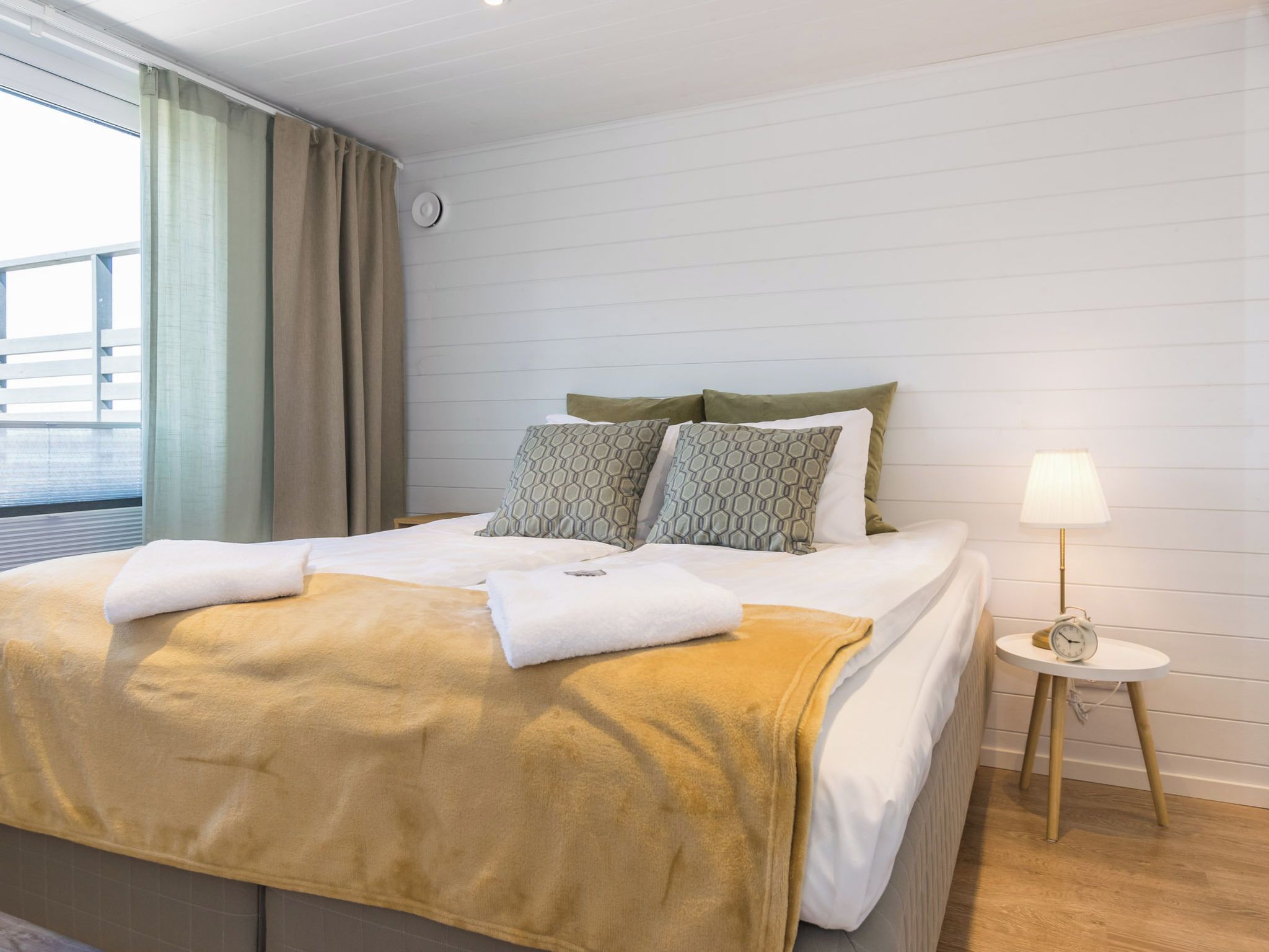 A hotel room with a bed, a bedside table with a lamp, and a view of the outside.