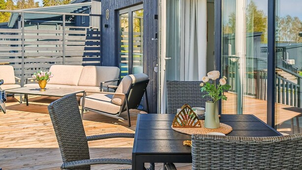 Une terrasse extérieure moderne, dotée de meubles en osier, d’une table et d’un vase de fleurs.