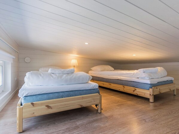A room with two wooden bunk beds, each with a mattress and pillows, and a bedside lamp.