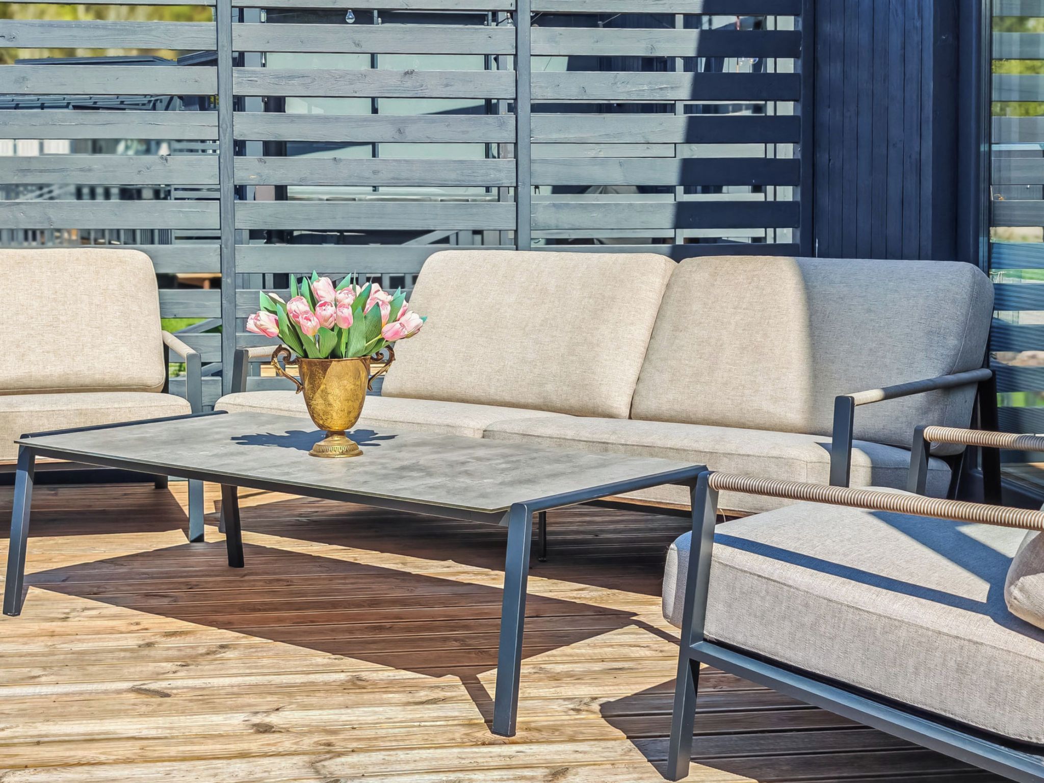 A deck with a sofa, two armchairs, a coffee table, and a vase with flowers.