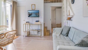 A modern living room with a sofa, a TV mounted on the wall, a wooden console table, and a wicker chair.