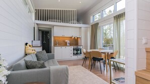 Ein modernes Wohnzimmer mit grauem Sofa, Couchtisch und Essbereich mit Tisch und Stühlen. Es gibt eine Küchenzeile mit Herd und Schränken.