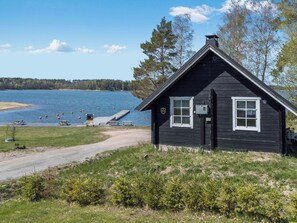 En stuga med en brygga som sträcker sig ut i en sjö, omgiven av träd och en klar himmel.