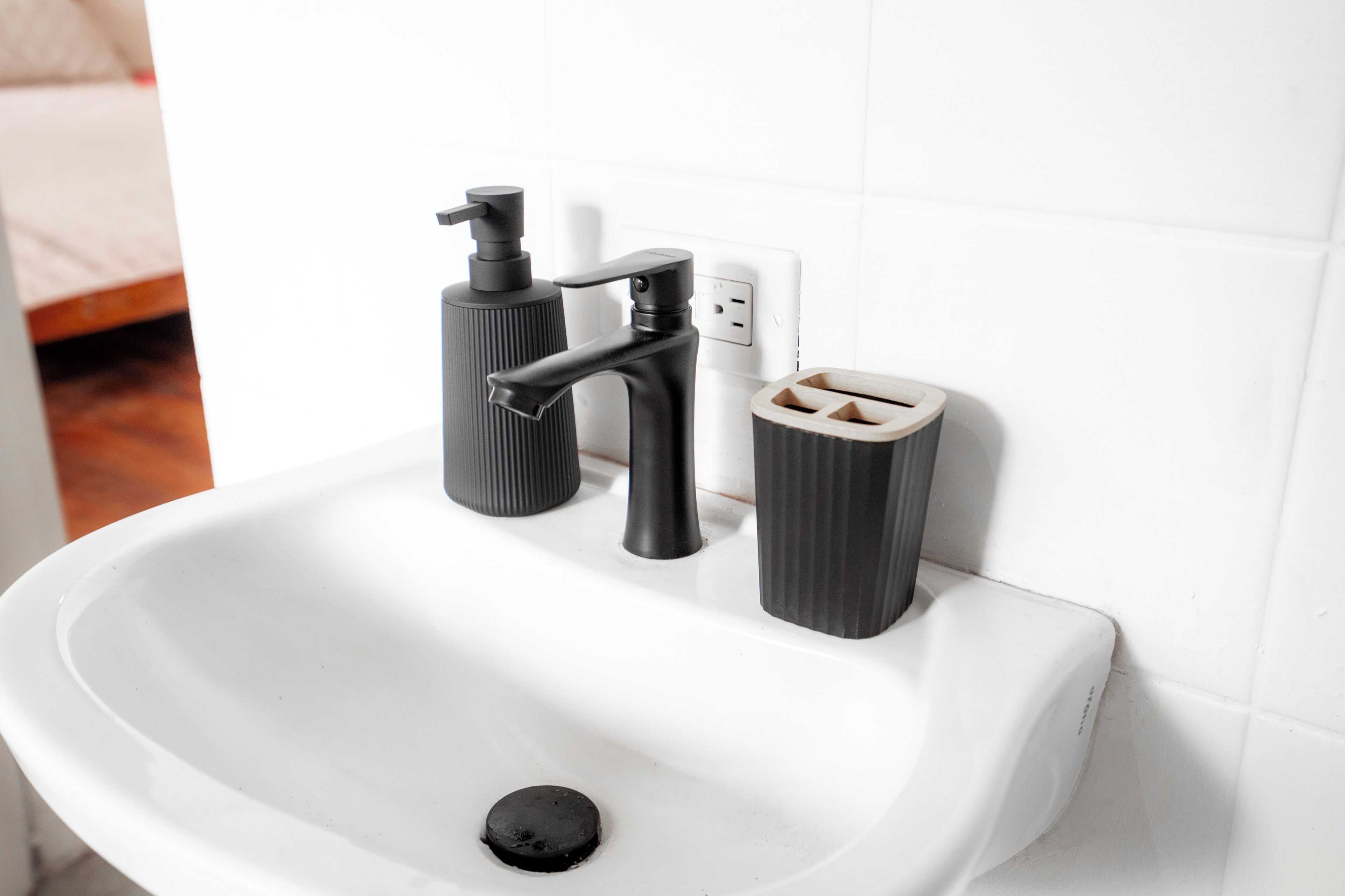 A white bathroom sink with a black faucet, a soap dispenser, and a toilet paper holder.