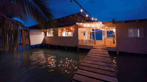 Een pand aan het water met houten looppaden, een overdekt terras en lichtjes.