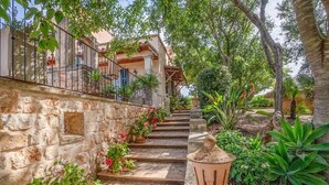 A stone staircase leading to a building with a balcony, surrounded by lush greenery and potted plants.