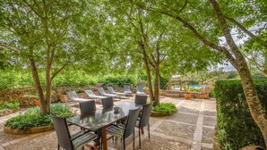 An outdoor patio with a table and chairs, surrounded by stone walls and greenery.