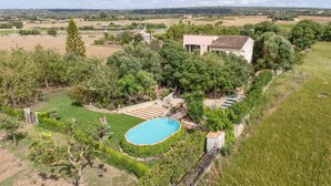 A large house with a swimming pool surrounded by lush greenery and a view of the countryside.