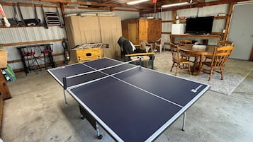 A ping pong table in a room with wooden furniture, a television, and a foosball table.