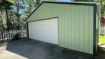 A green garage with a white door, surrounded by trees and a white picket fence.