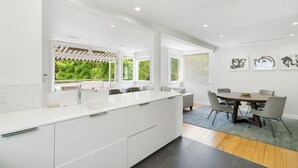 Une cuisine moderne avec des meubles blancs, un grand îlot central et un coin repas comprenant une table et des chaises.
