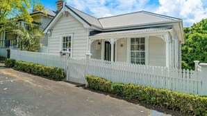 Une maison blanche à deux étages, avec une clôture en bois peinte en blanc, un porche couvert et une cheminée.