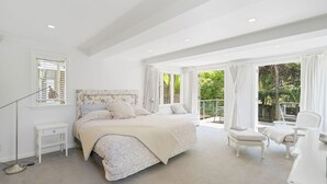 Une chambre spacieuse avec un grand lit, une table de chevet, une lampe sur pied et une vue sur l’extérieur grâce à de grandes fenêtres.