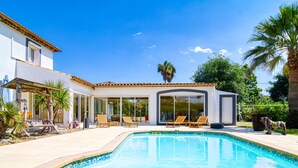 A modern house with a swimming pool, sun loungers, and a covered patio area.