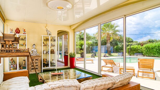 A spacious living room with a large glass door leading to a pool area, wooden furniture, and a decorative cabinet with figurines.