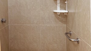 A shower area with beige tiles, a white shelf, and a grab bar. - Habitación Independiente al Norte de Mérida (Mérida)