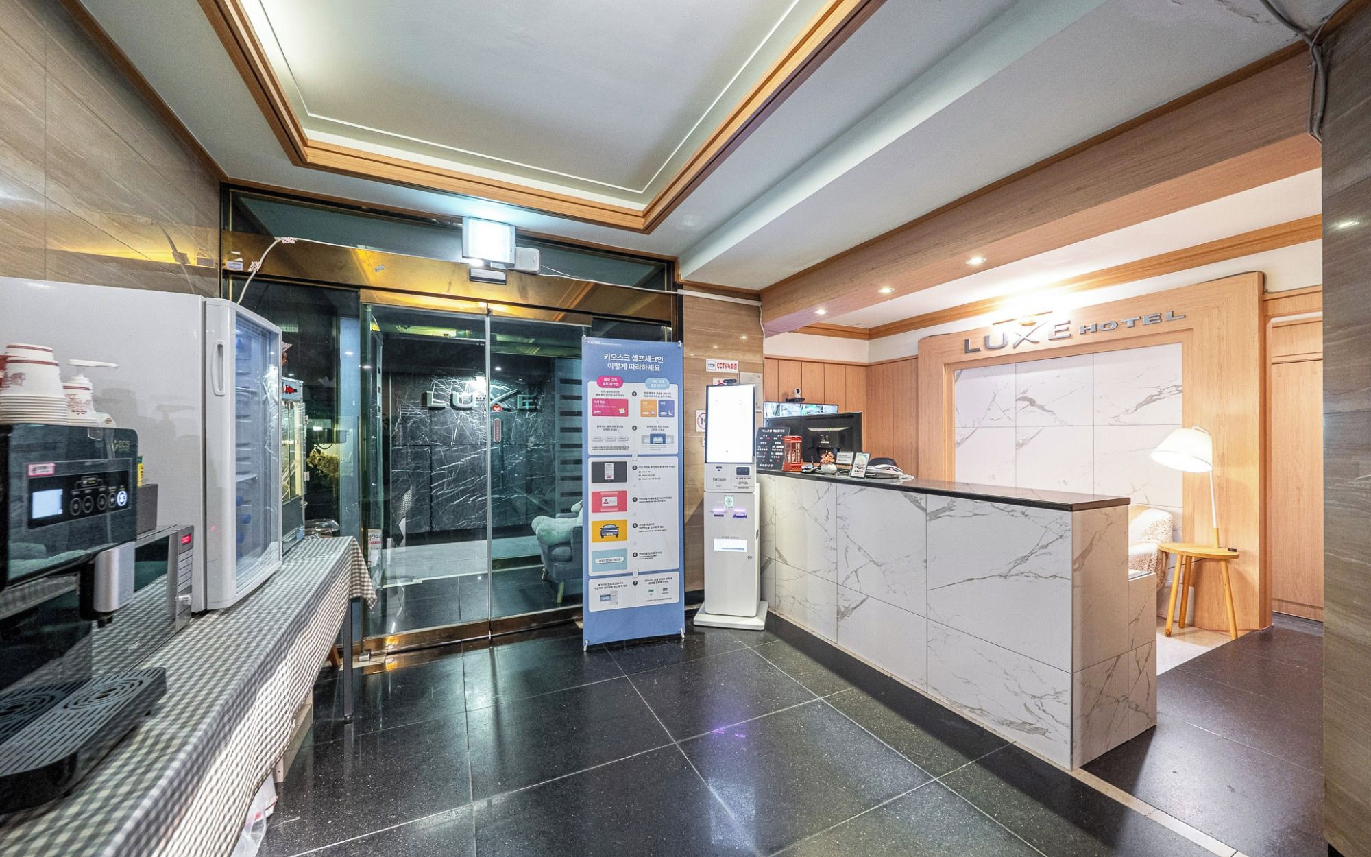 A hotel reception area with a marble counter, a coffee machine, and a glass door entrance.