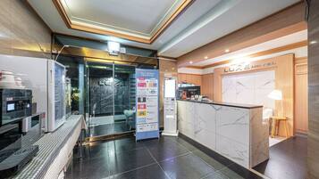 A hotel reception area with a marble counter, a coffee machine, and a glass door entrance.