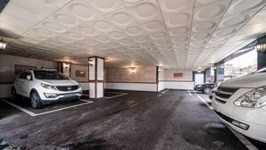 A parking garage with two cars parked, a textured ceiling, and wall-mounted lights. - Nowon Luxe hotel (Seoul)