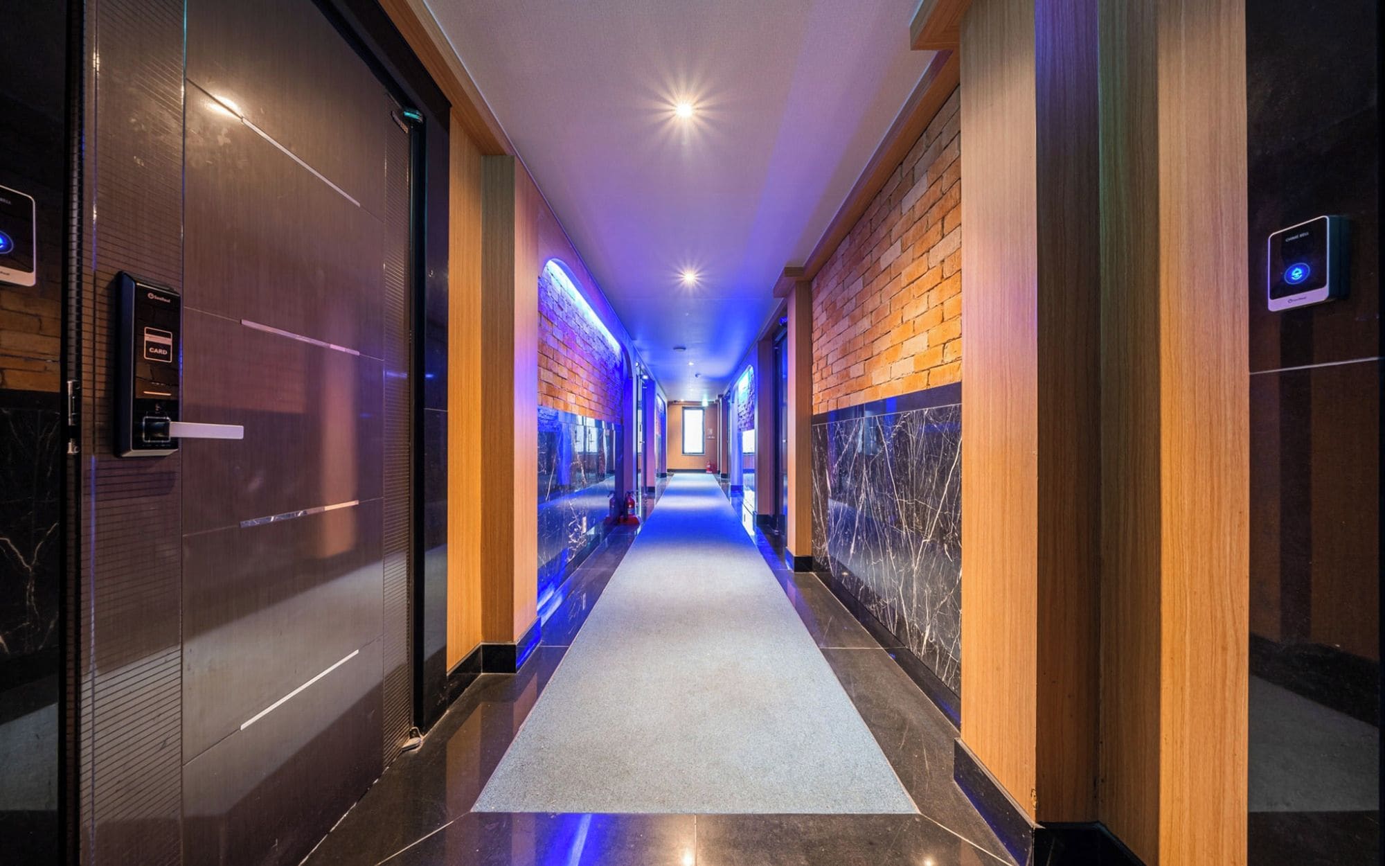 A hotel corridor with a marble floor, wooden walls, and a blue-lit ceiling.