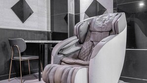 A massage chair with a cushioned seat and backrest, a small table, and a chair with a metal frame. - Nowon Luxe hotel (Seoul)