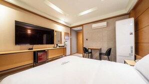 A hotel room with a bed, a TV, a mini-fridge, a desk, two chairs, and an air conditioning unit. - Nowon Luxe hotel (Seoul)