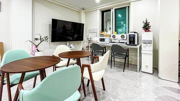 A modern dining area with a flat-screen TV, a kitchen with a microwave, and a small Christmas tree.