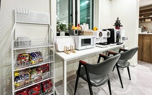 A modern kitchen with a microwave, toaster, and coffee maker on the counter. There are two chairs and a small Christmas tree on the right. - Nowon Luxe hotel (Seoul)