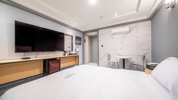 A modern hotel room with a large bed, a flat-screen TV, a desk with a coffee machine, and a small table with chairs.