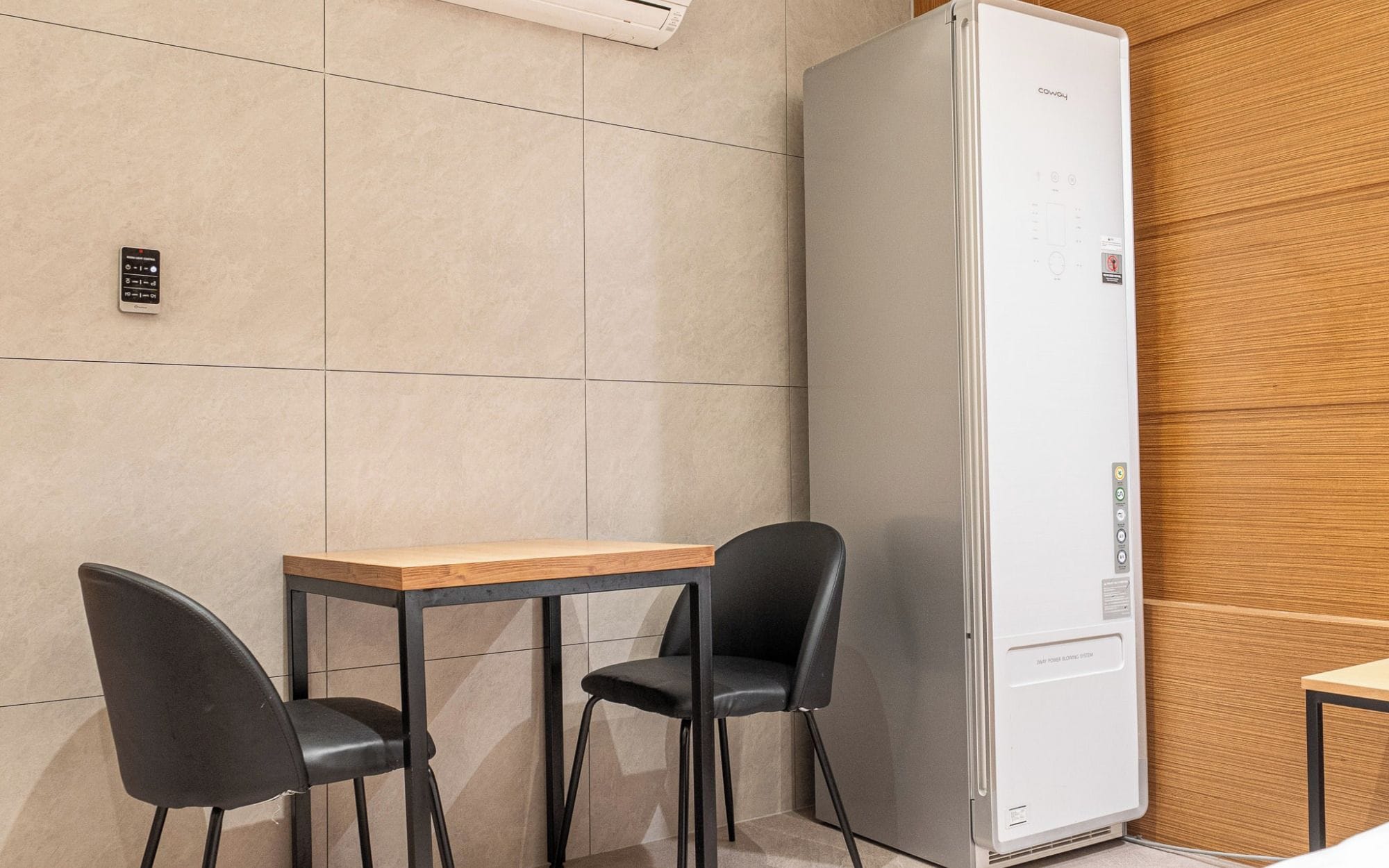 Une petite cuisine équipée avec un réfrigérateur blanc, une petite table et deux chaises noires.