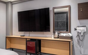 Habitación de hotel con televisión de pantalla plana, espejo, secador de pelo, tetera y un pequeño armario rojo.