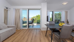 A modern living room with a sofa, a dining table with chairs, and a balcony with a view of the city. - 1 bedroom beautiful apartment in Malinska (Malinska)