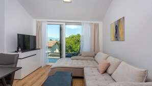A modern bedroom with a large bed, a TV, a desk, and a balcony with a view of greenery and buildings. - 1 bedroom beautiful apartment in Malinska (Malinska)