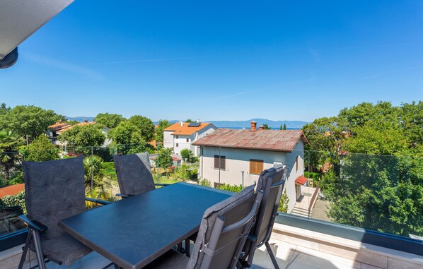 A balcony with a table and chairs, overlooking a residential area with houses and trees.