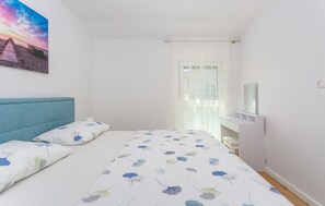 A bedroom with a bed, a headboard, a bedside table, a mirror, and a window with curtains.