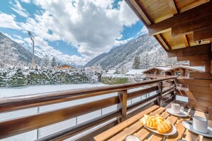 A wooden balcony with a view of snow-covered mountains and a clear sky.