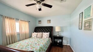 A bedroom with a bed, a nightstand, a ceiling fan, and a window with curtains. - FLIP FLOP INN, 5MIN TO CRUISE AND BEACH (Galveston)