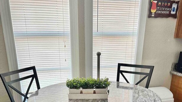 A round marble table with four black chairs, a small plant centerpiece, and a window with blinds in the background. - FLIP FLOP INN, 5MIN TO CRUISE AND BEACH (Galveston)