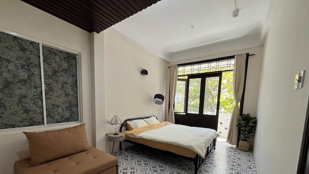 A bedroom with a bed, a sofa, a small table, and a window with curtains. - Lanni House (Da Nang)