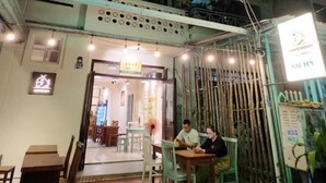 An outdoor seating area with tables and chairs, a covered entrance, and a sign indicating the name of the establishment. - Lanni House (Da Nang)