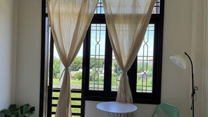 A room with a window, a small round table, a green chair, and a potted plant. - Lanni House (Da Nang)