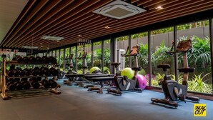 Ett gym med träningsutrustning, stänger för vikter och stora fönster med utsikt över grönområden.