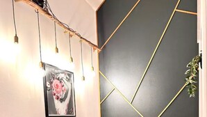 Et moderne interiør med et glasbord, to pink polstrede stole, en mørk væg med geometriske gyldne linjer, og en base af træstub.